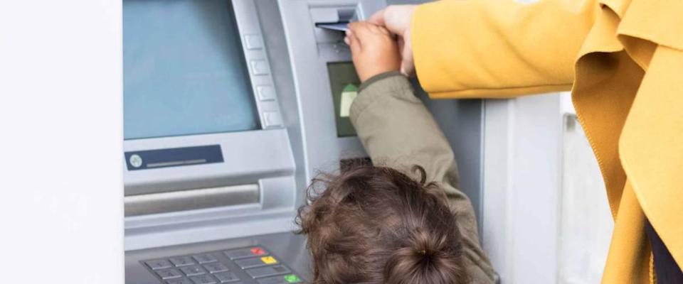 Mother and daughter standing at cash machine, putting in card