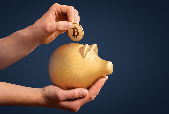 Person putting Bitcoin token into a piggy bank