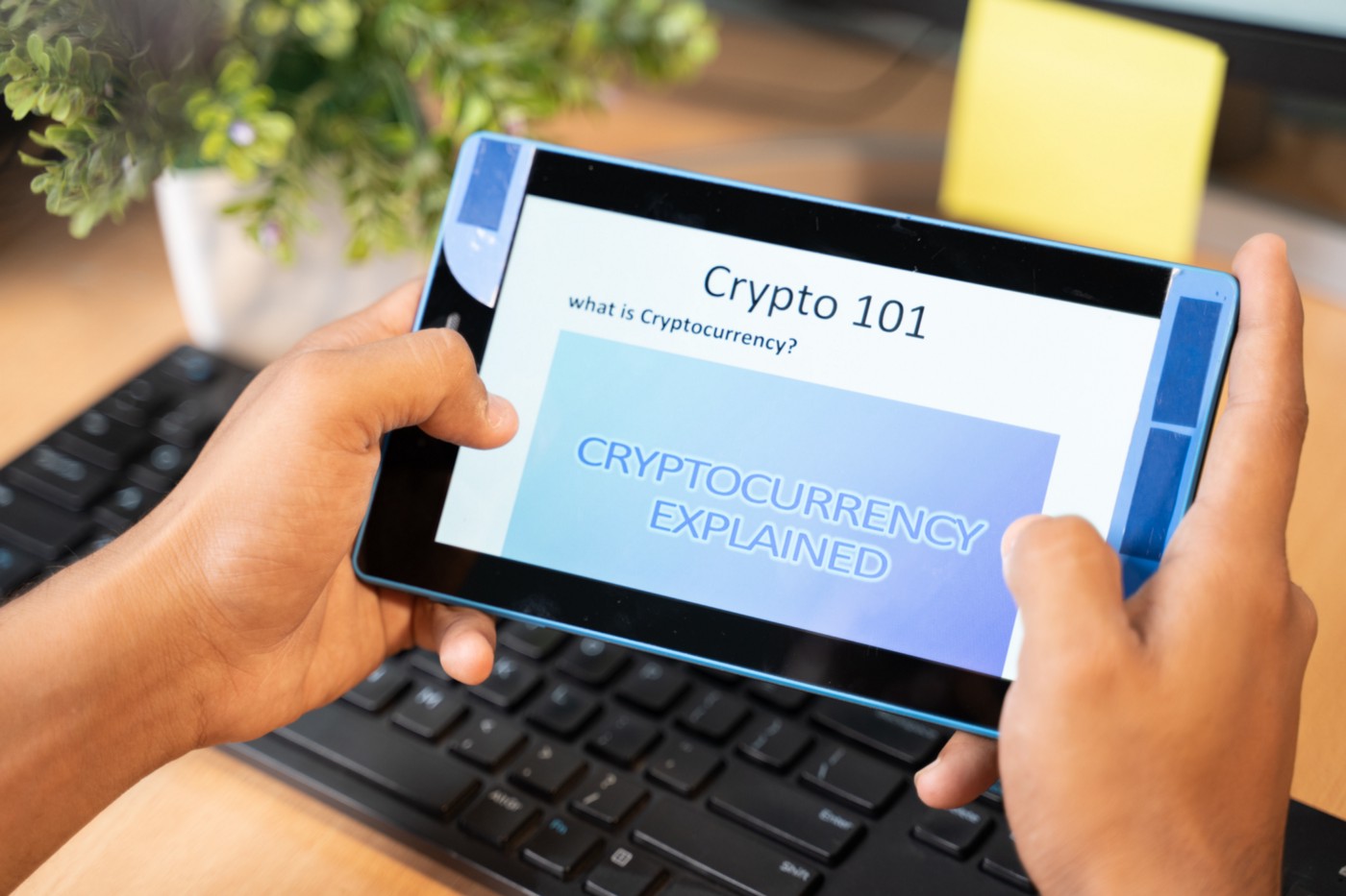 Shows someone holding a tablet with the words Crypto 101 & Cryptocurrency Explained.